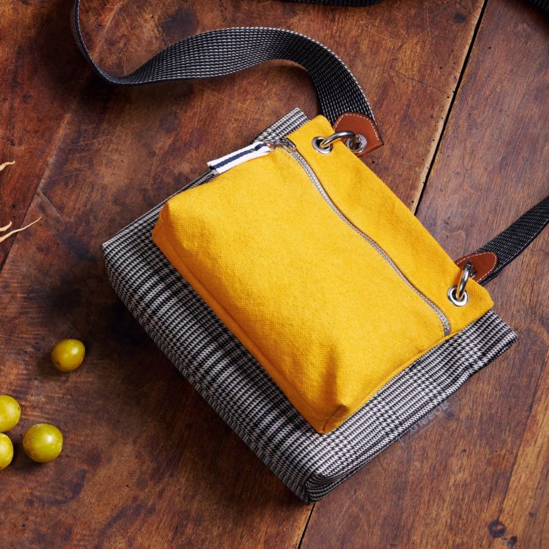 pochette yole en coton jaune accrochee à un equipier polyester prince de Galles et à une sangle grisee posée sur une table en bois avec des mirabelles